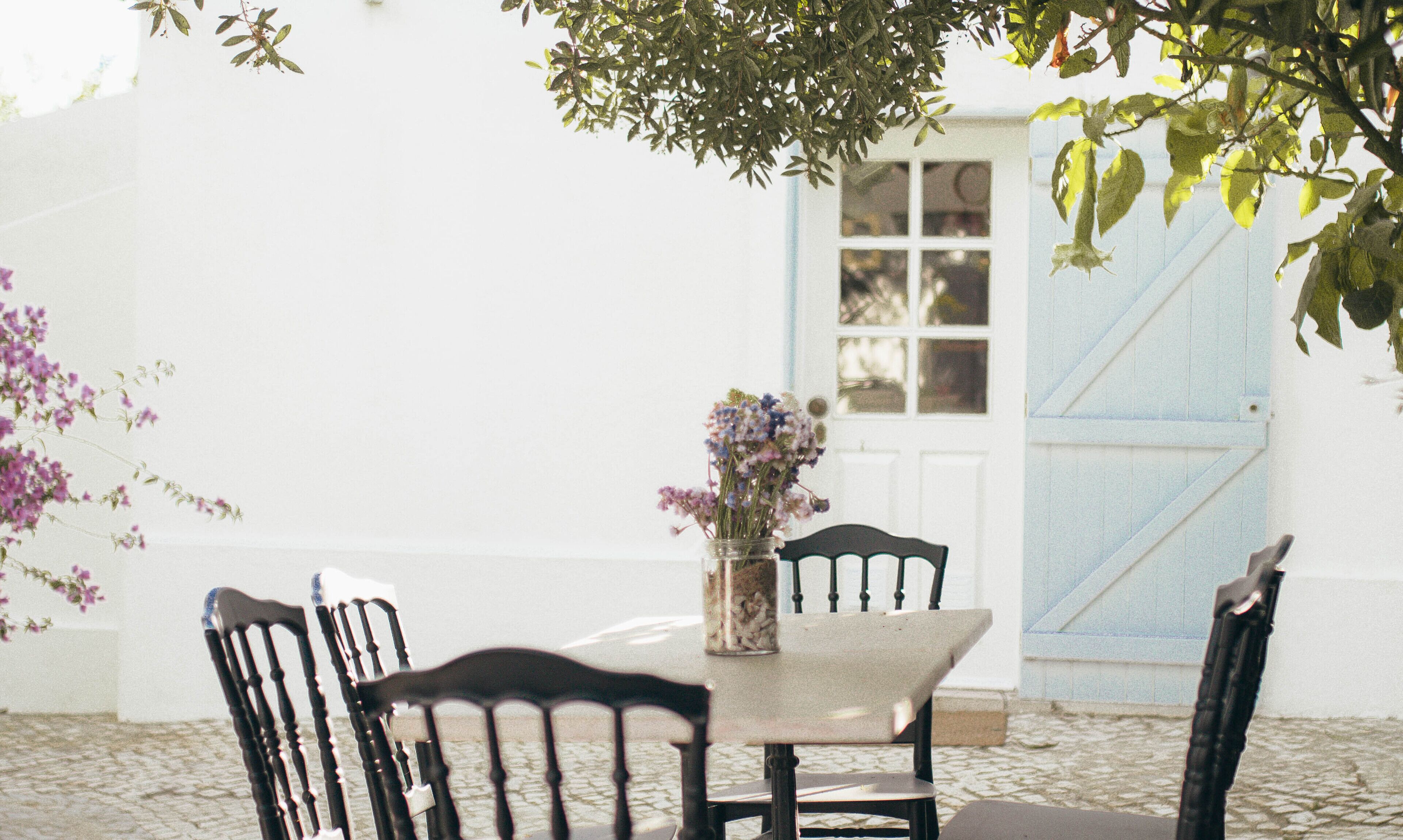 A table with chairs, a vase with flowers, and a blue door in the background.