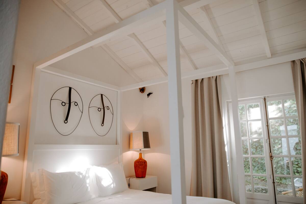 Un dormitorio con cama, mesita de noche, lámpara y ventana con cortinas.
