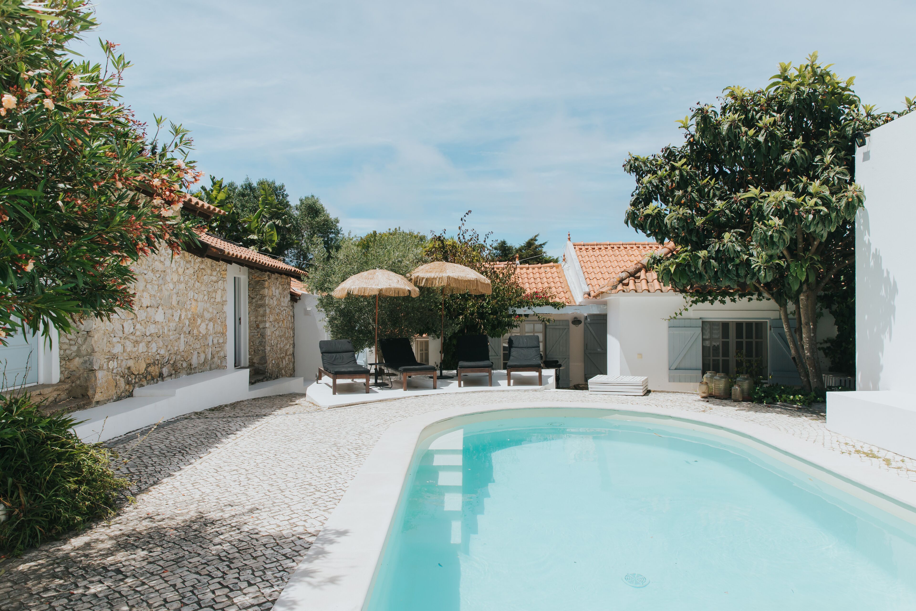 Une piscine entourée de murs de pierre et de verdure, avec des chaises longues et des parasols.