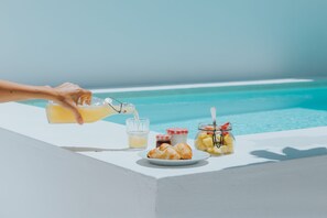 A table with a glass of orange juice, a plate with croissants, and jars of jam and fruit by a pool. - Senhora do Cabo Meco (Sesimbra)