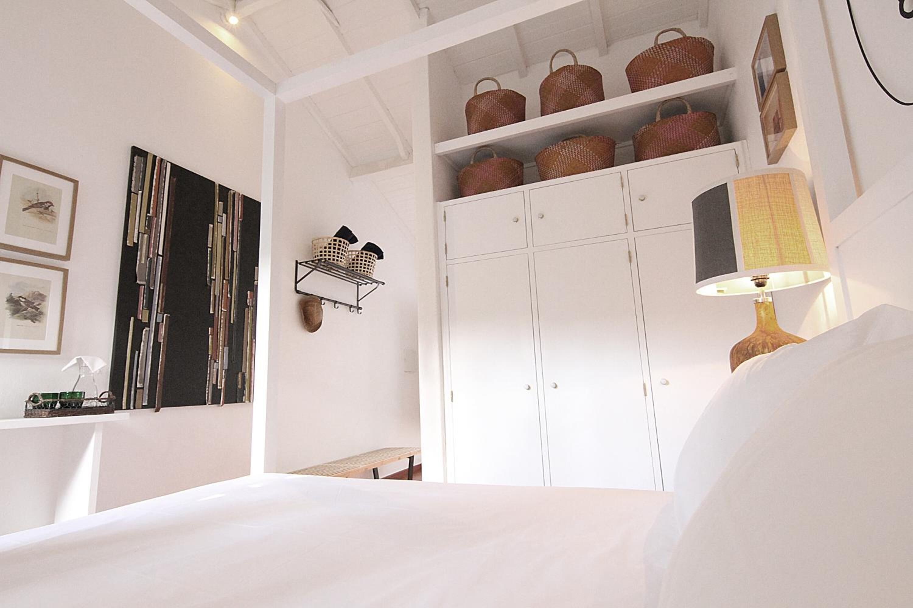 A bedroom with a bed, a bedside table, a lamp, a wardrobe, and shelves with baskets.