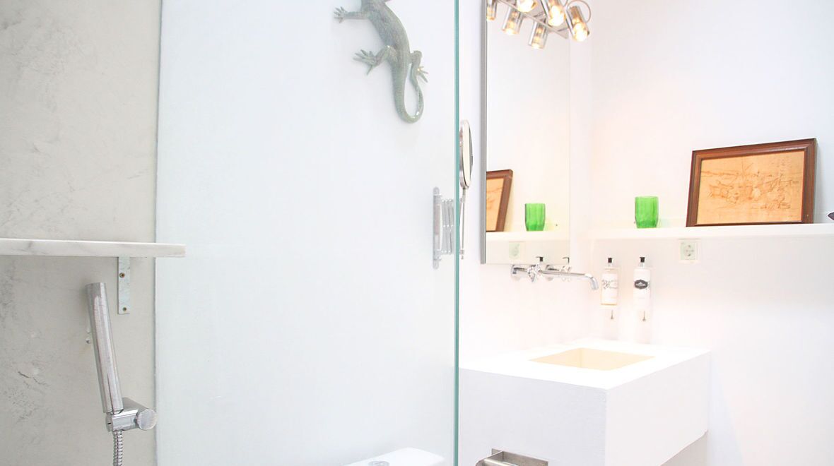 Un baño con cabina de ducha de vidrio, un lavabo blanco y un espejo con un cuadro enmarcado.