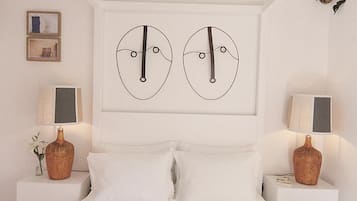Un dormitorio con una cama blanca, dos mesitas de noche con lámparas y dos obras de arte abstracto en la pared.