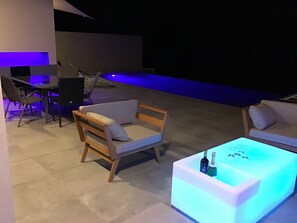 An outdoor seating area with a pool, a table with bottles, and chairs.