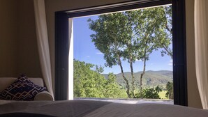 Ein Schlafzimmer mit großem Fenster und Blick auf bewaldetes Gelände und Hügel.