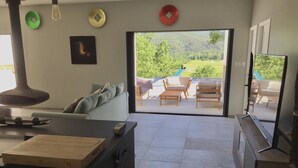 Ein modernes Wohnzimmer mit einer Couch, einem Couchtisch und einem Fernseher. Eine Glastür öffnet sich zu einer Terrasse mit Pool und Gartenmöbeln.