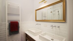 Ein Badezimmer mit zwei Waschbecken, einem Spiegel mit goldener Rahmung und einem Handtuchhalter mit roten und grauen Handtüchern.