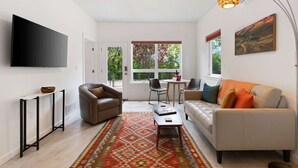 A modern living room with a sofa, chairs, a coffee table, a TV, and a patterned rug.