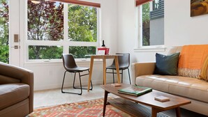 A living room with a beige sofa, two chairs, a coffee table, and a window with a view of trees.