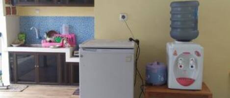 A compact kitchen with a refrigerator, a water dispenser, and a microwave on a wooden shelf.