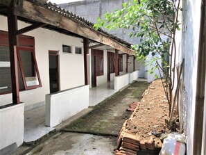 Um corredor com paredes brancas e janelas emolduradas a vermelho, que leva a uma área coberta com chão ladrilhado.