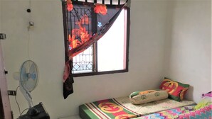 Une petite pièce simple, avec deux lits, une fenêtre munie d’une grille en métal, un ventilateur sur pied et une prise électrique au mur.
