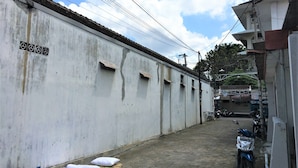 Une ruelle étroite avec un mur en béton, une moto garée sur le côté droit et un bâtiment avec une enseigne visible au fond.