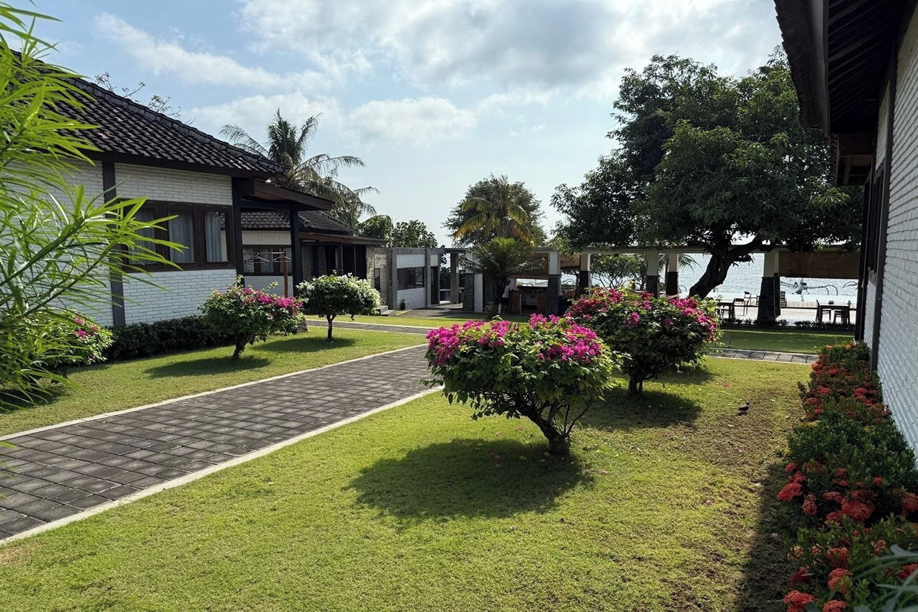 A pathway leading to a building with a tiled roof, surrounded by well-maintained grass and flowering bushes.