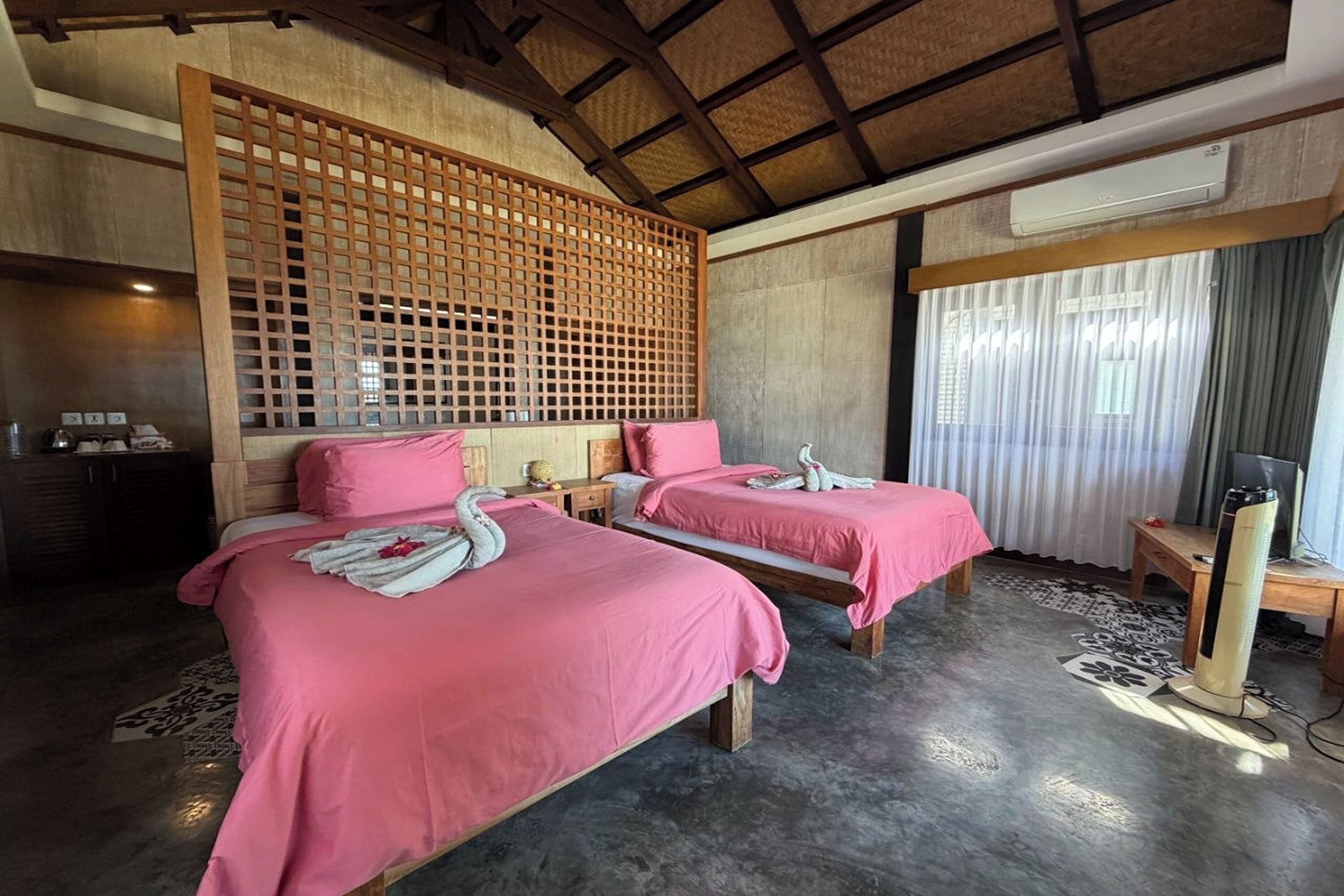 Una habitación con dos camas, un separador de madera, un aire acondicionado, un televisor y una alfombra estampada.