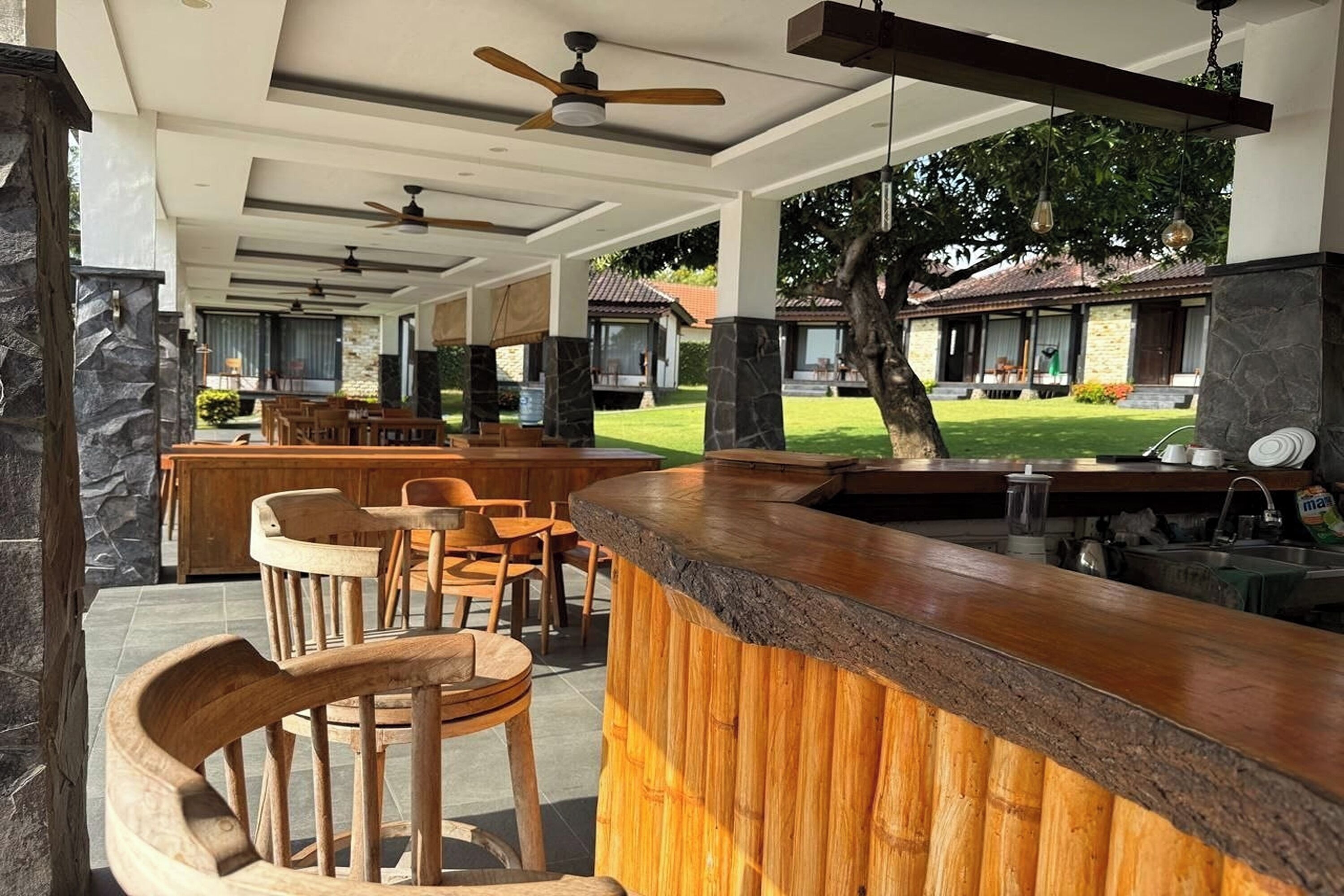 A covered outdoor seating area with wooden furniture, a stone column, and a bar counter.