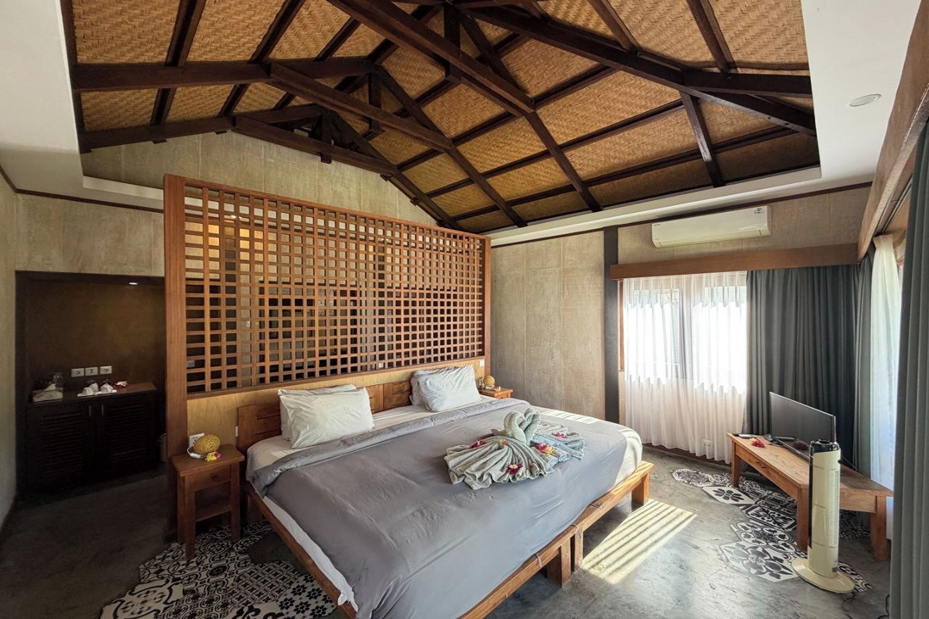 Un dormitorio con cama, cabecero de madera, mesitas de noche, televisor y ventana con cortinas.