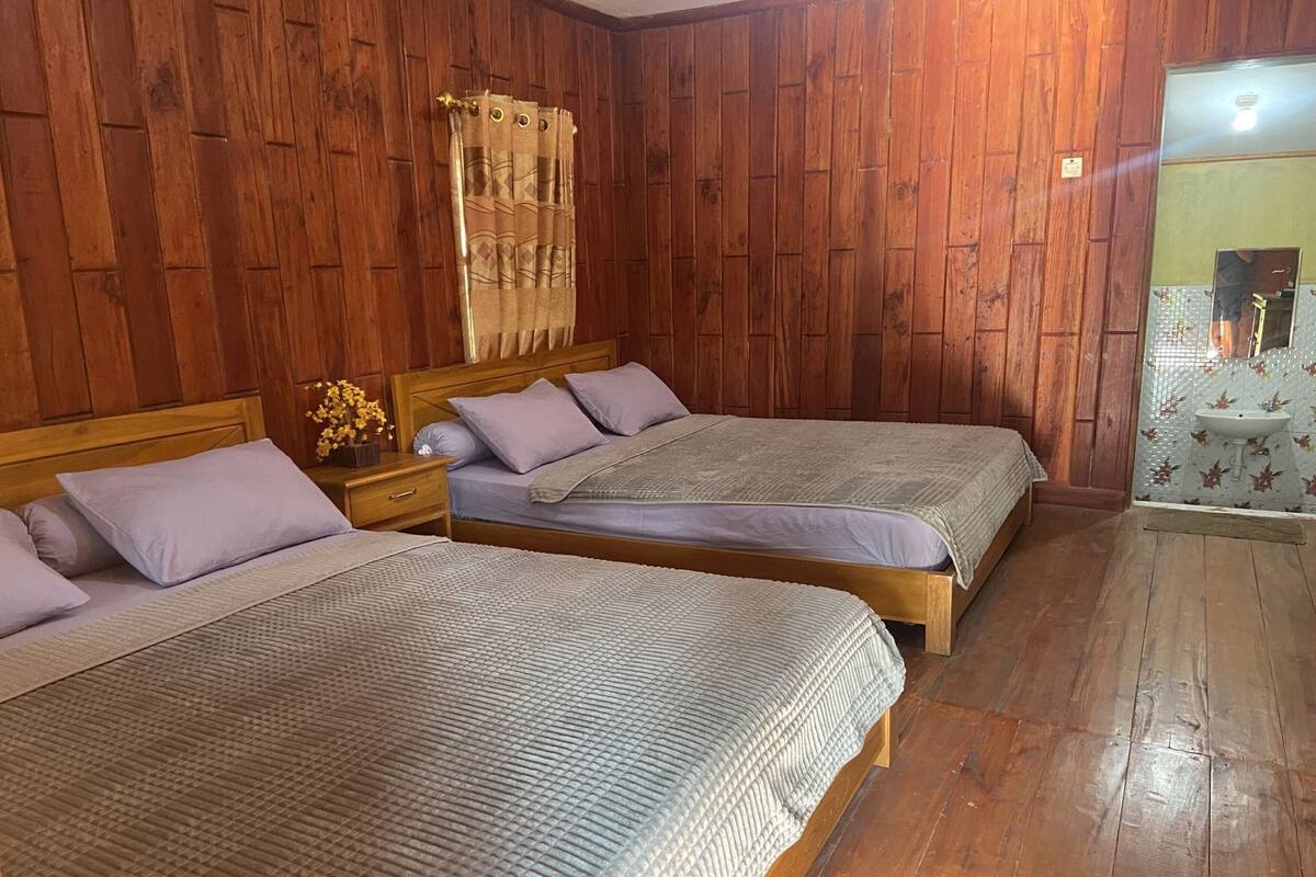 Een kamer met houten wanden, twee bedden met bijpassende hoofdeinden, een nachtkastje met een lamp en een badkamer met een wastafel en spiegel.