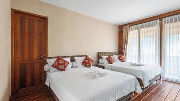 A hotel room with two beds, wooden flooring, a large wooden door, and a window with curtains.