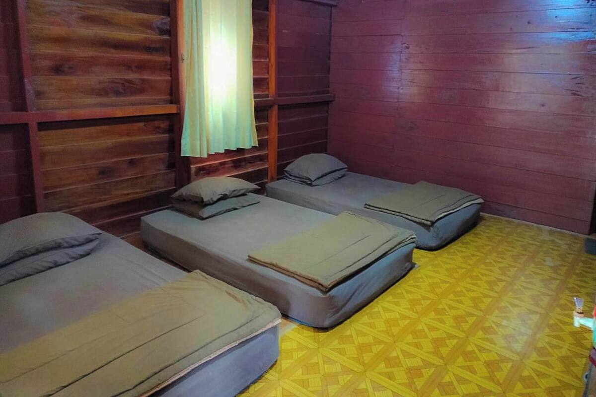Een kamer met drie eenpersoonsbedden, houten wanden, een geel patroon vloer en een raam met gordijn.