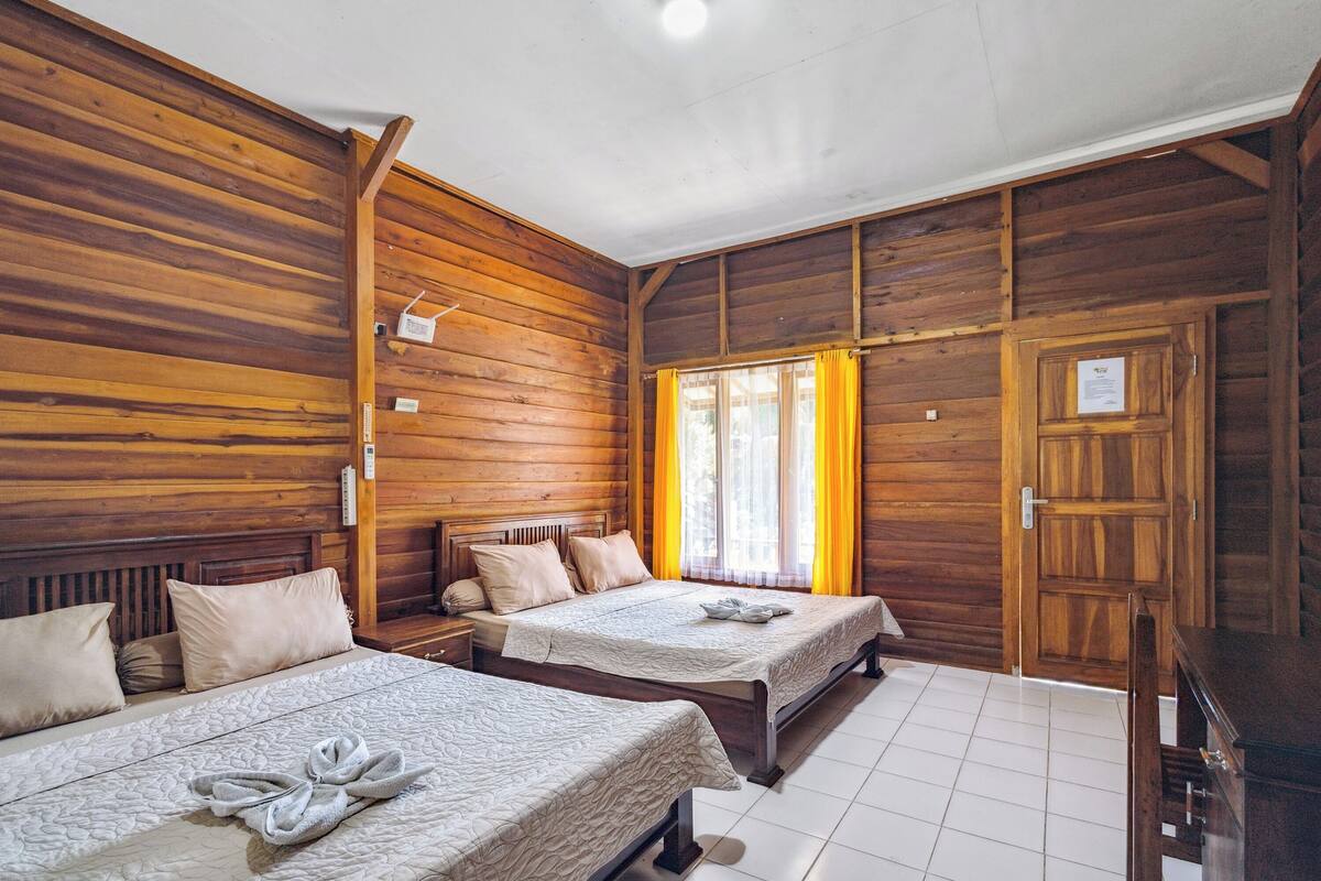 Een houten kamer met twee bedden, een raam met gele gordijnen en een houten deur.