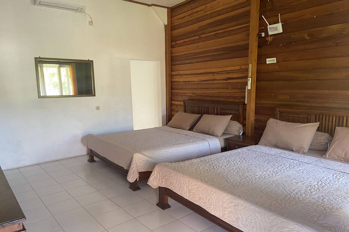 Een kamer met twee bedden, een raam en een houten wand.