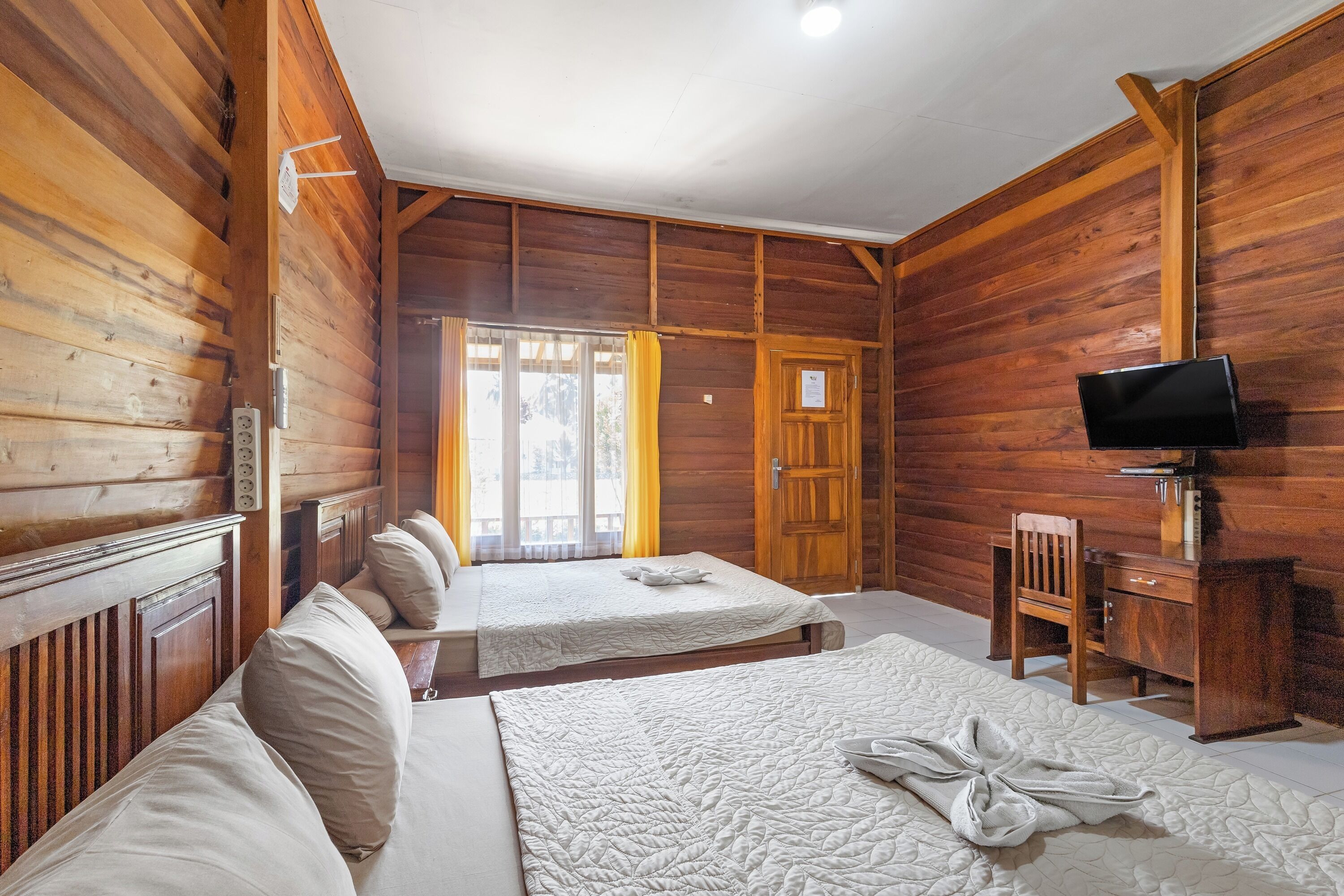 Una habitación tipo cabaña de madera con dos camas, un escritorio y un televisor.