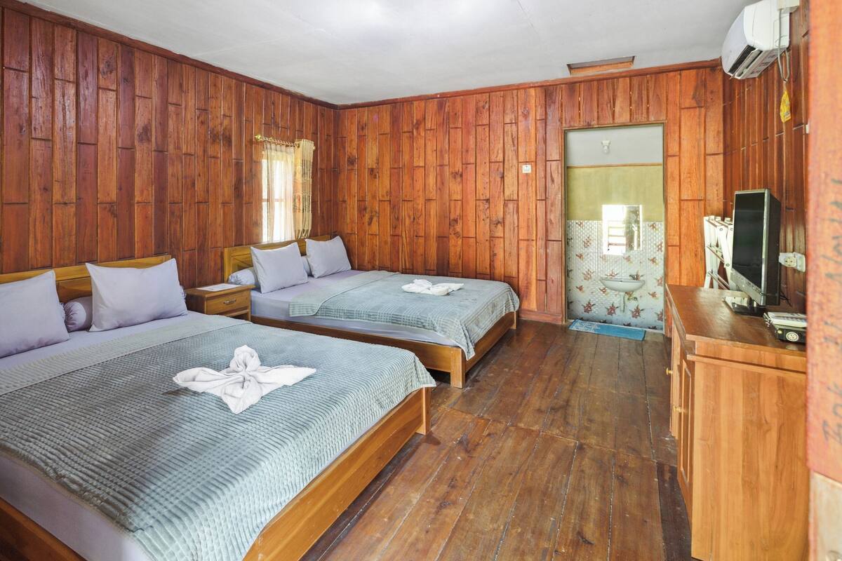 Een kamer met twee houten bedden, een klein nachtkastje, een televisie en een badkamers deur.