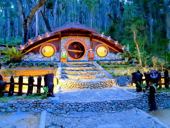 Un arco rústico de piedra que da paso a una estructura de madera con un ventanal circular y dos faroles a cada lado.