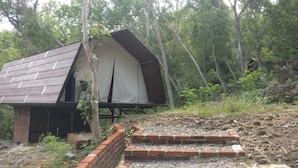A small, rustic cabin with a sloped roof and a brick foundation, surrounded by dense forest. - Seribu Batu Songgo Langit Resort & Camp (Mangunan)