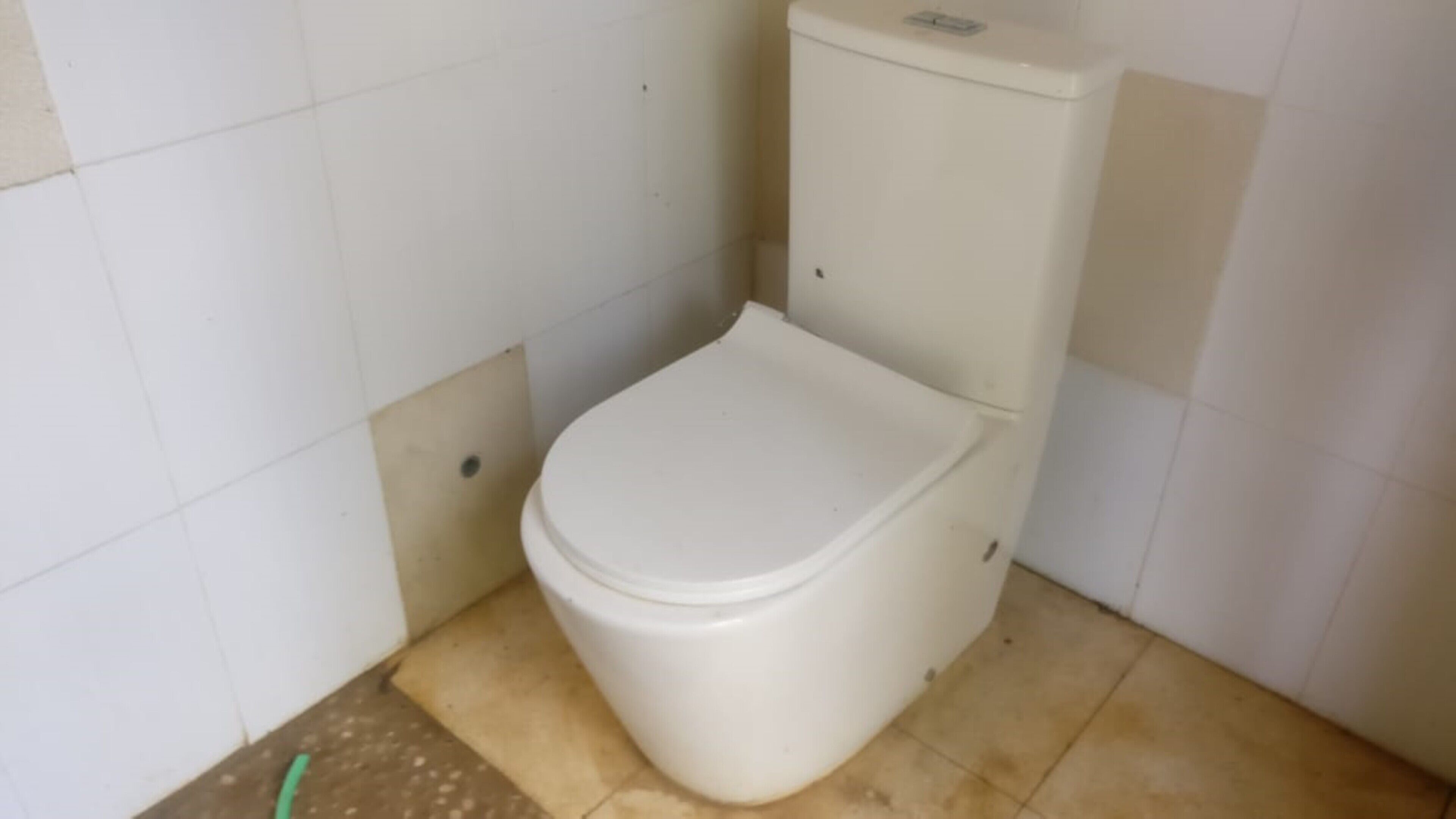 A small, white toilet in a bathroom with white tiled walls and a brown floor.