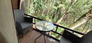 Un balcón con sillas de mimbre y una mesa de vidrio, con vista a un bosque denso.