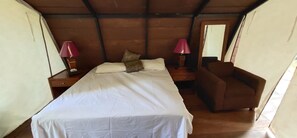 Un dormitorio con una cama, dos mesitas de noche, una silla y un espejo.