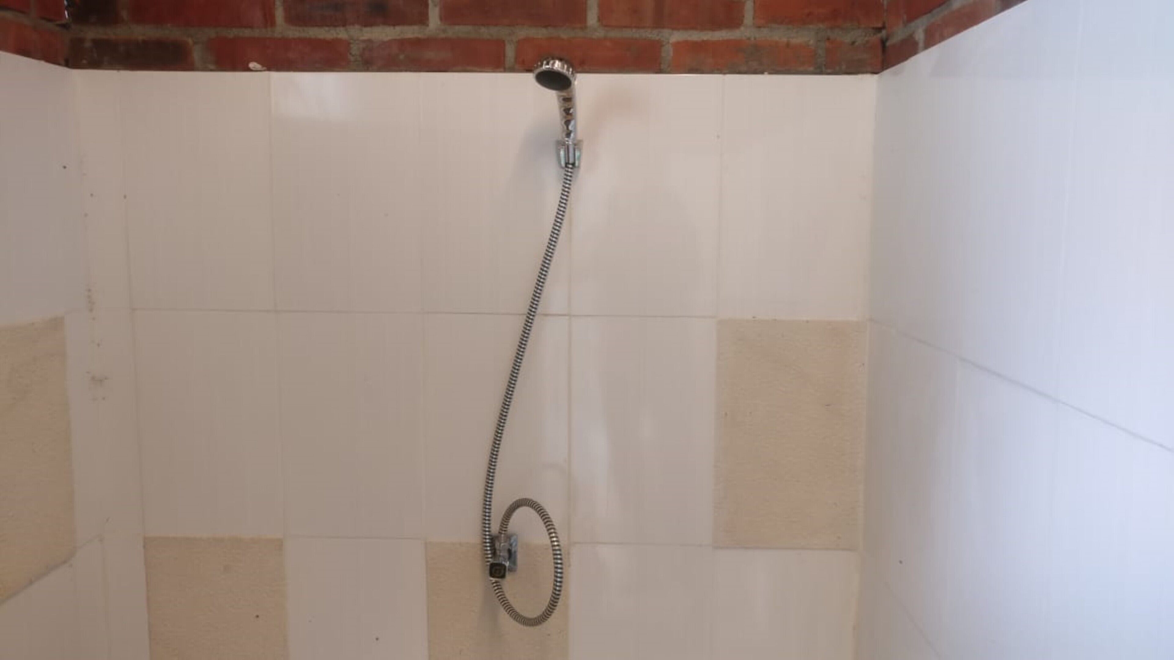 A shower with a hose, tiled walls, and a brick wall at the top.