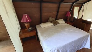 A bedroom with a bed, two bedside lamps, a nightstand, and a wooden headboard. - Watu Mabur Holiday Centre and Camping (Mangunan)