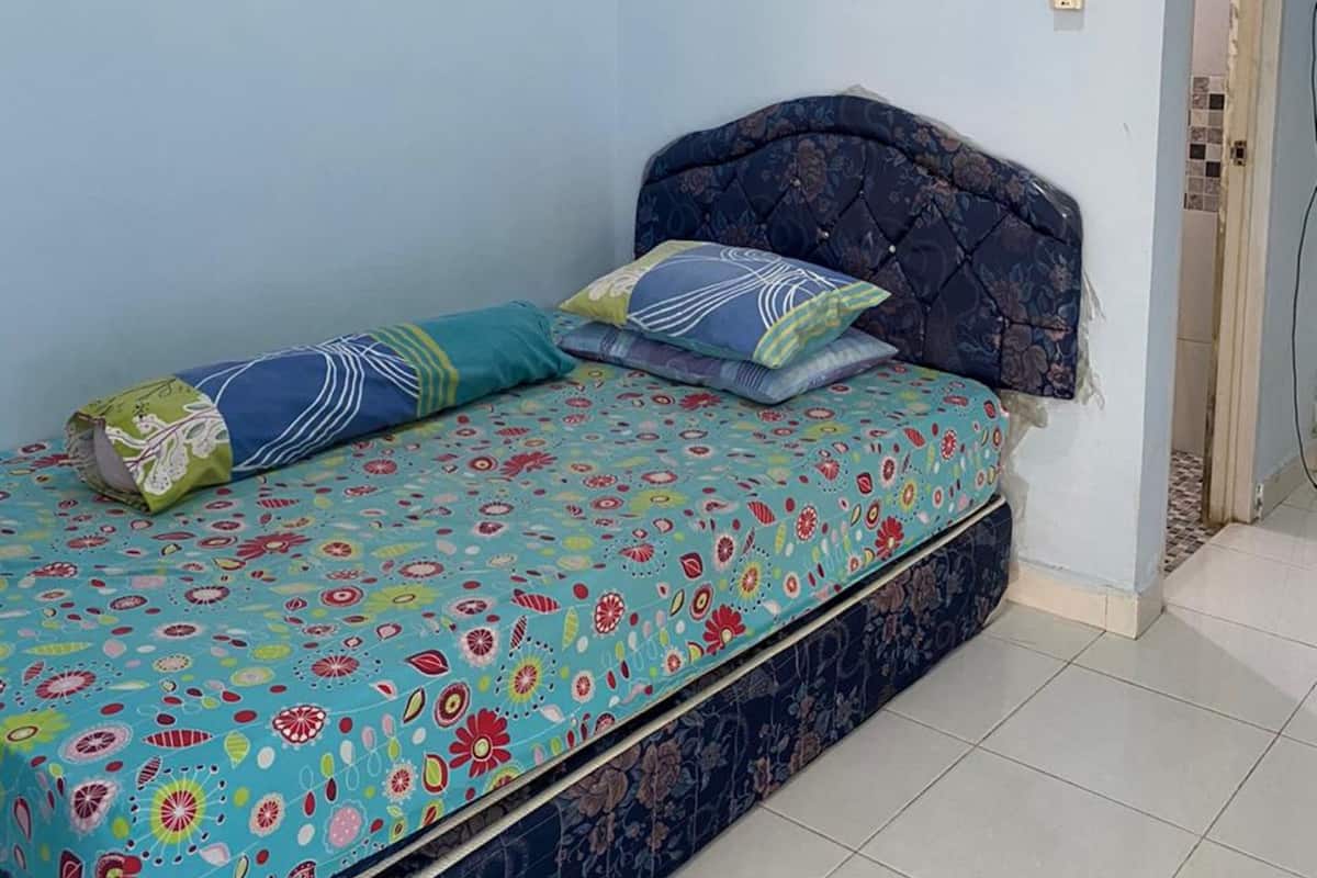 Un lit simple avec une couvre-lit à motifs floraux, une tête de lit et deux oreillers.