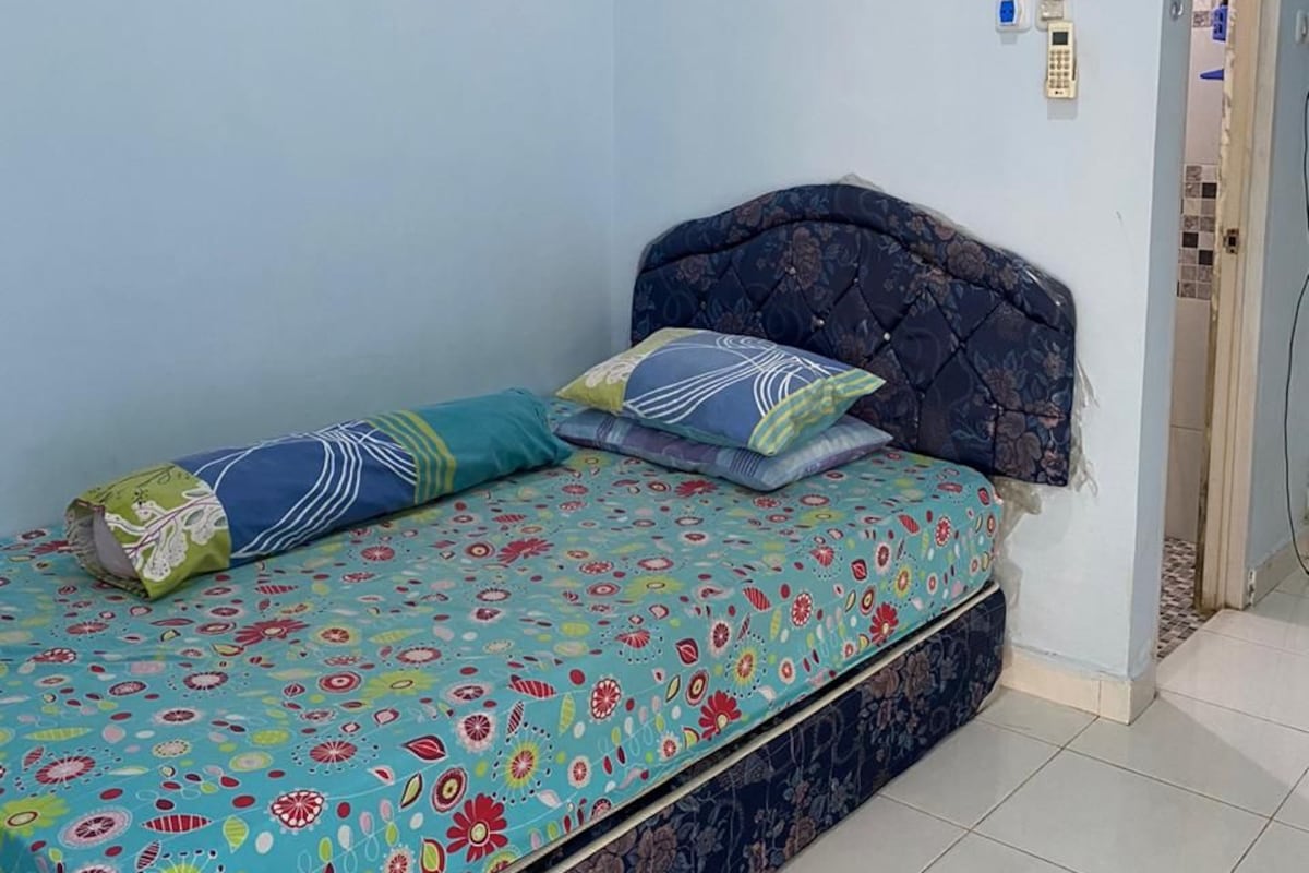 Ein Bett mit floralem Überwurf, einem dunklen Kopfteil und zwei Kissen.