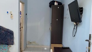 Une petite pièce comprenant un lit, un bureau, une armoire, un téléviseur et une porte.