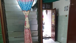 A room with a window covered by a floral curtain, green tiled walls, and a tiled floor. - Homestay Mas Arjuna - Female Only (Surabaya)