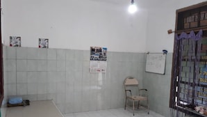 A room with a tiled floor, a whiteboard, a calendar, and a chair. - Homestay Mas Arjuna - Female Only (Surabaya)