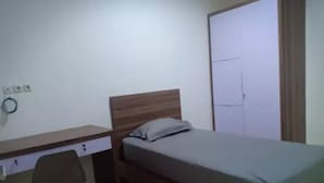 A bedroom with a wooden bed, a desk with a chair, and a wardrobe. - Kost Harian 86 (Surabaya)