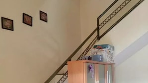 A staircase with a metal railing, a wooden cabinet with glass doors, and several cardboard boxes. - Kost Harian 86 (Surabaya)