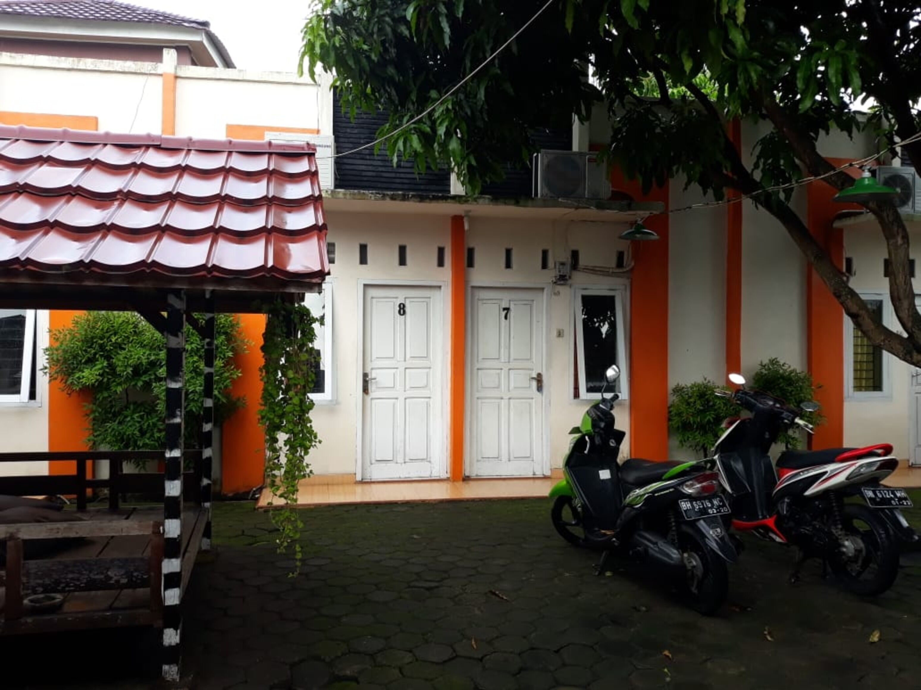 A courtyard with a tiled roof structure, two white doors, and a motorcycle parked in front.