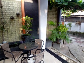 A patio area with a round table and wicker chairs, surrounded by potted plants and a small dog. - Dedy Kost (Jambi)
