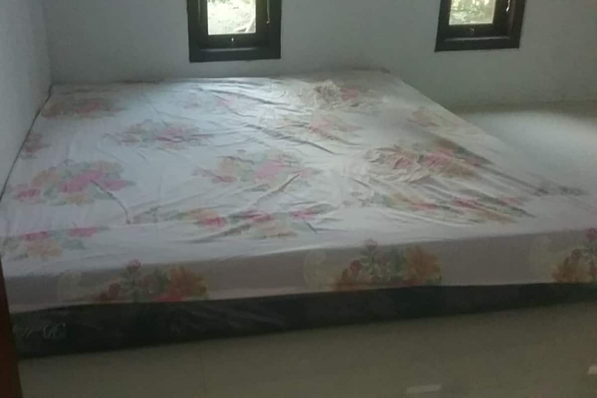 A room with a bed covered in floral-patterned bedding, two windows, and a plain wall.