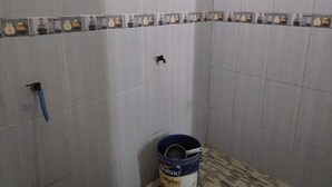 A bathroom with grey tiled walls, a decorative border with fruit patterns, a blue bucket, and a faucet. - Dwi Sigit Homestay (Imogiri)