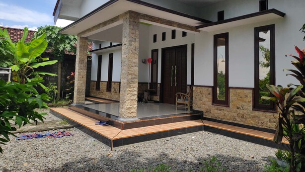 A two-story house with a covered porch, stone pillars, and a tiled roof. - Dwi Sigit Homestay (Imogiri)