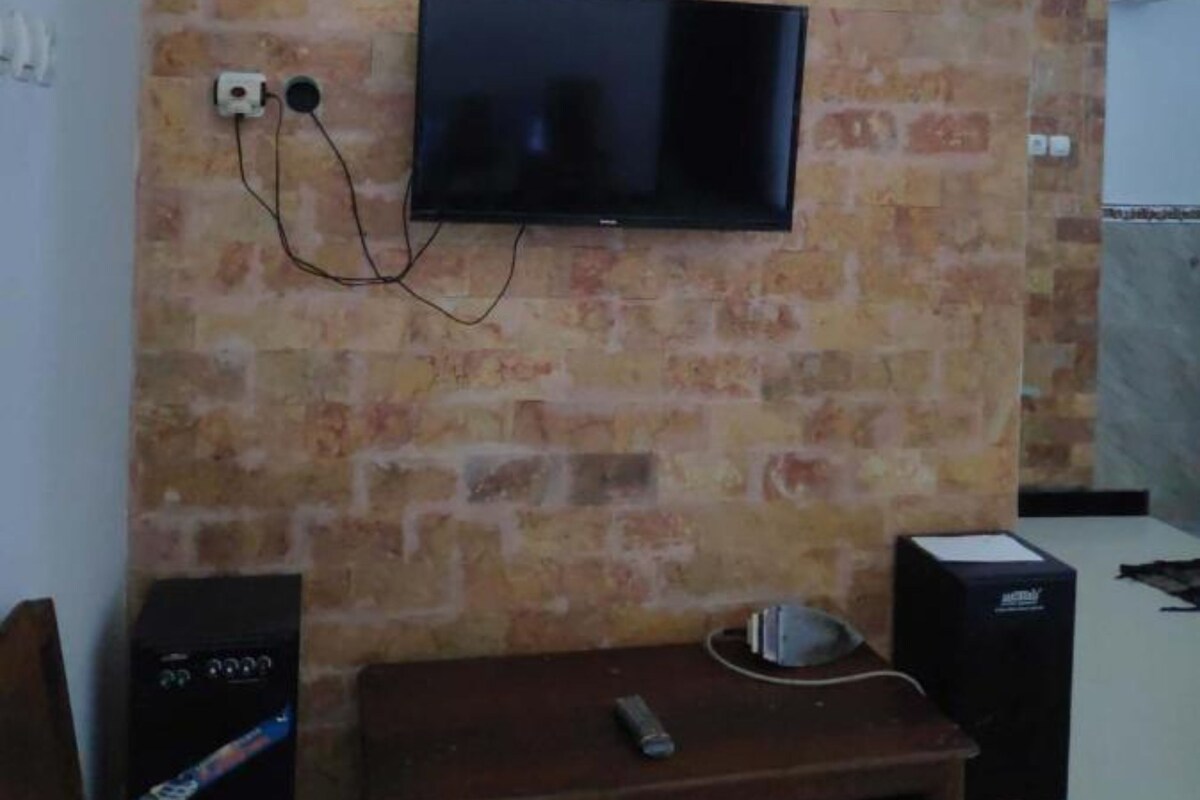 Ein Zimmer mit Backsteinwand, einem an der Wand befestigten Flachbildfernseher, einem Holztisch und einem Lautsprecher.