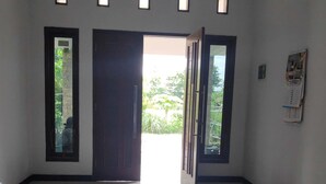 A hallway with a polished floor, a door leading outside, and a bulletin board on the wall. - Dwi Sigit Homestay (Imogiri)