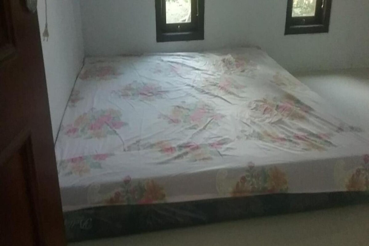 Una habitación con una cama cubierta por una colcha estampada, dos ventanas y una puerta.